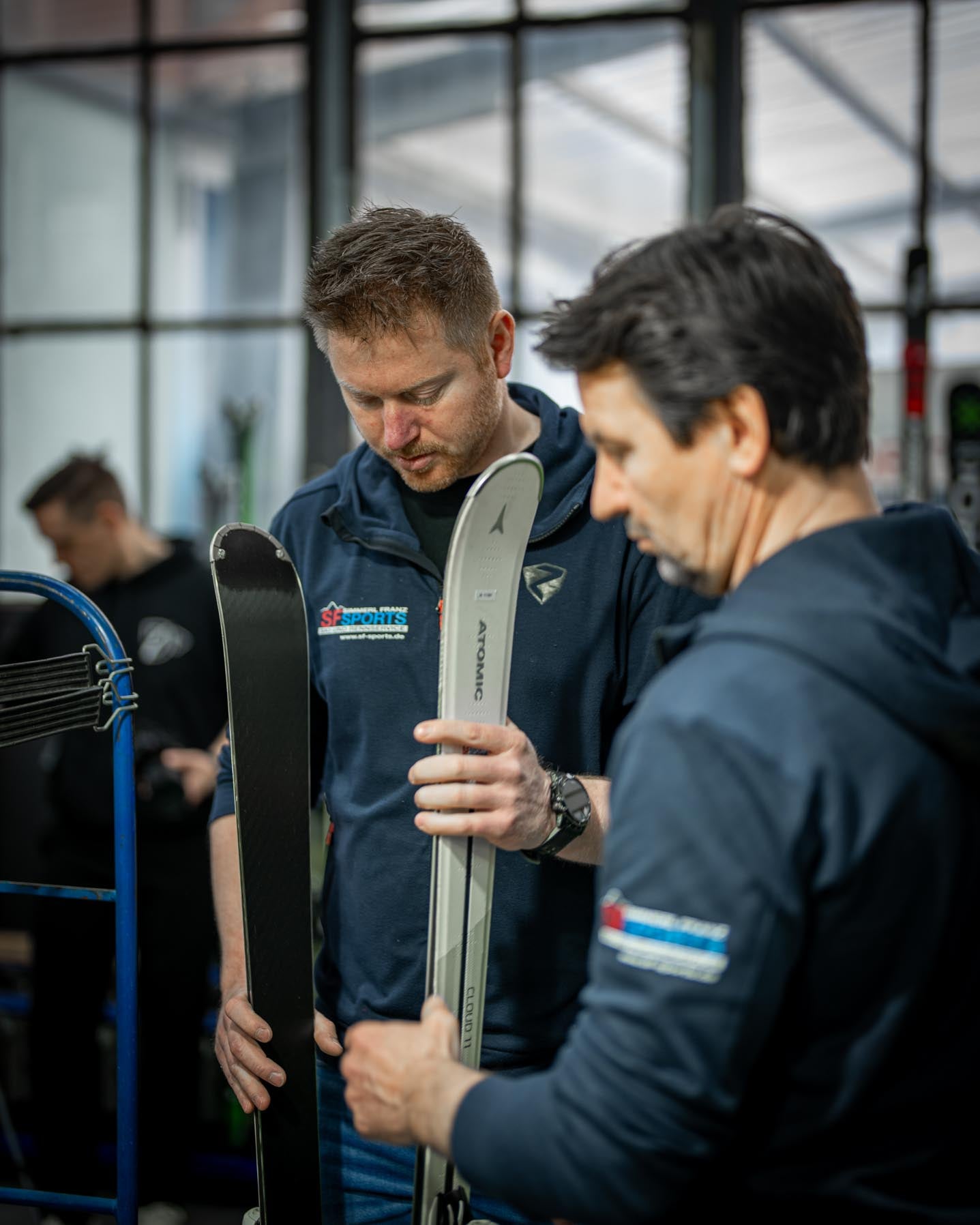 Franz Simmerl hält zwei Paar Skier in der Hand, die für den Rennservice bei SF Sports präpariert werden. Die Szene zeigt die Expertise und Präzision, mit der Rennski für optimale Performance im Wettkampf vorbereitet werden.